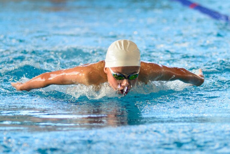 Swimmer boy swims butterfly swimming style in the pool. Closeup