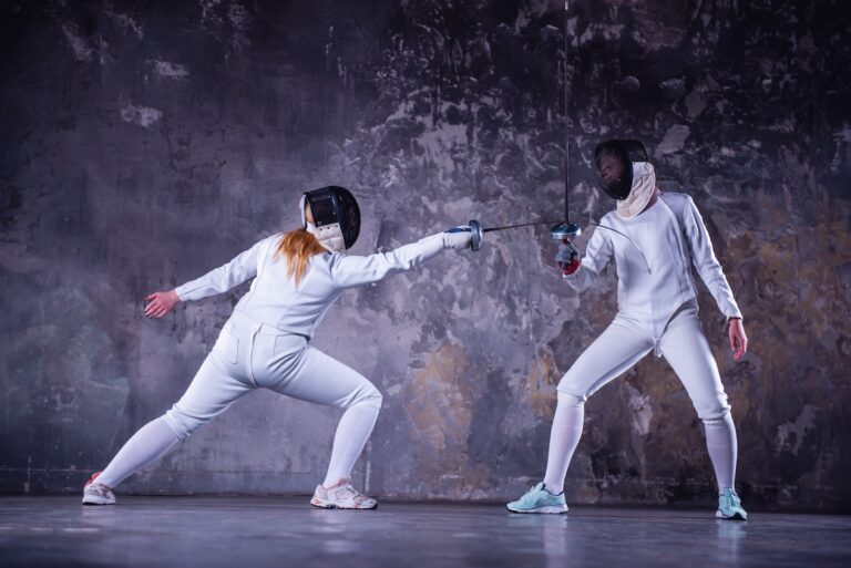 Female fencers in protective clothing are fighting on dark gray background, full-length