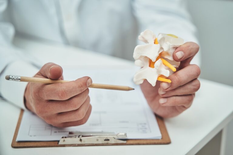 Cropped photo of a doctor with a pencil in his hand demonstrating a basic vertebra model for patient education